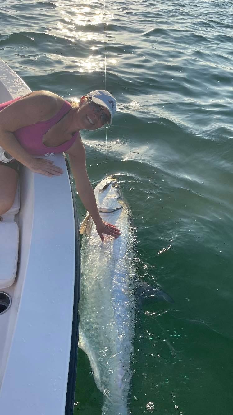 A woman is standing on the side of a boat holding a fish.