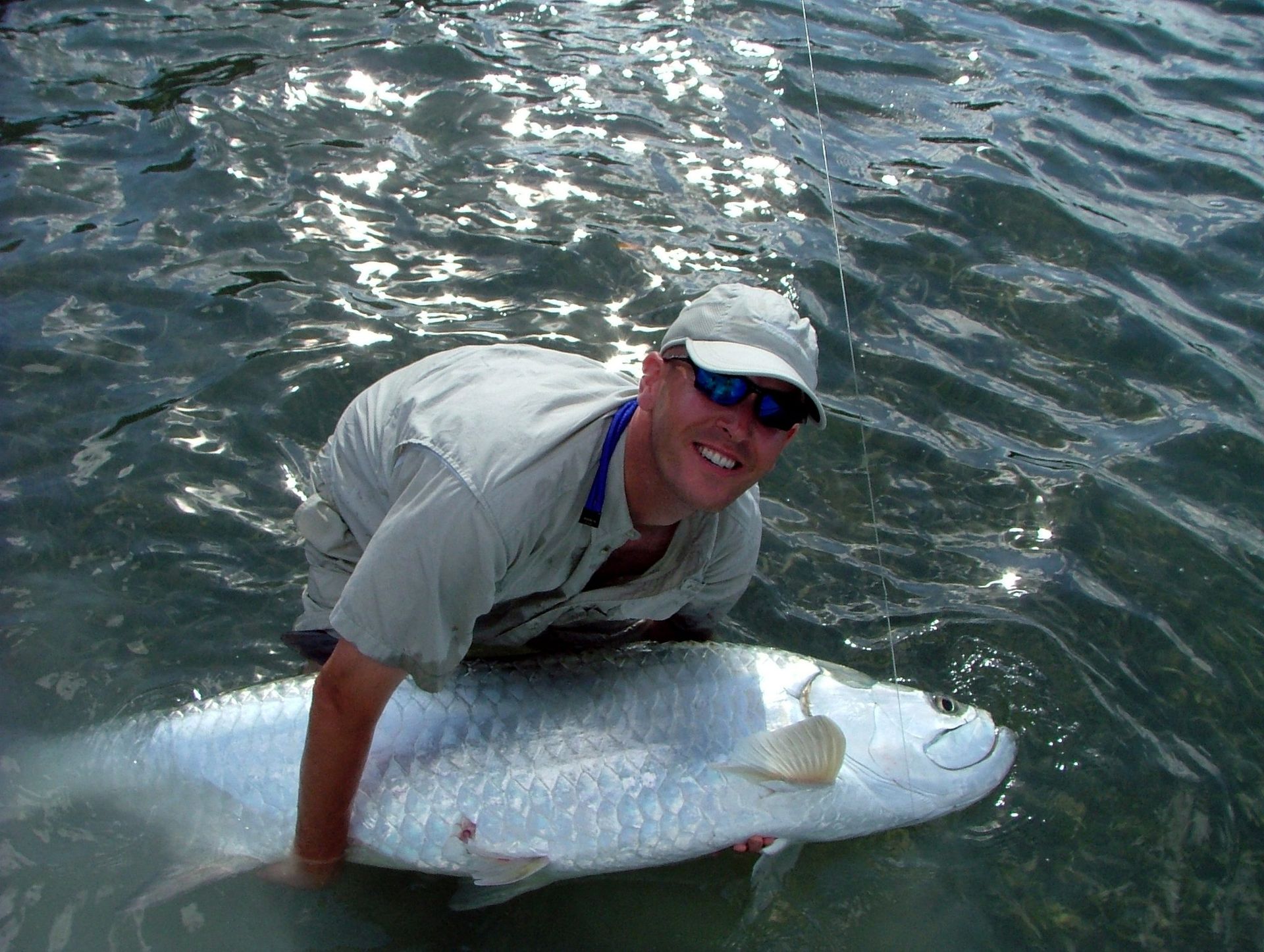 A man is kneeling in the water holding a large fish