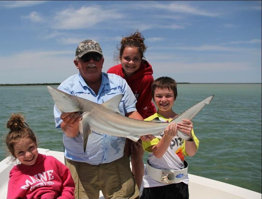 A group of people holding a shark on a boat with one wearing a shirt that says alone