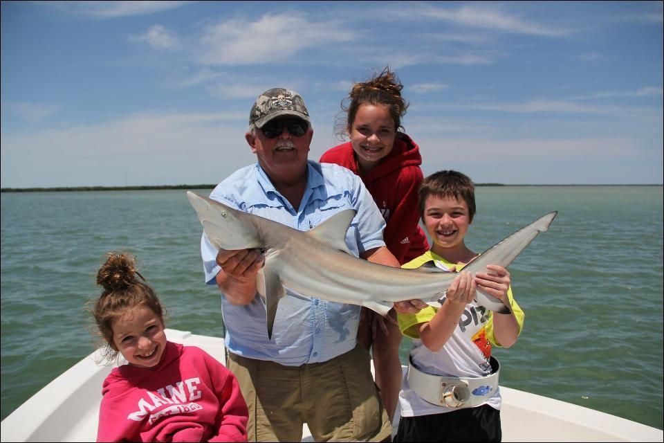 Family on a boat holding a small shark they caught. Sunny day, open water.