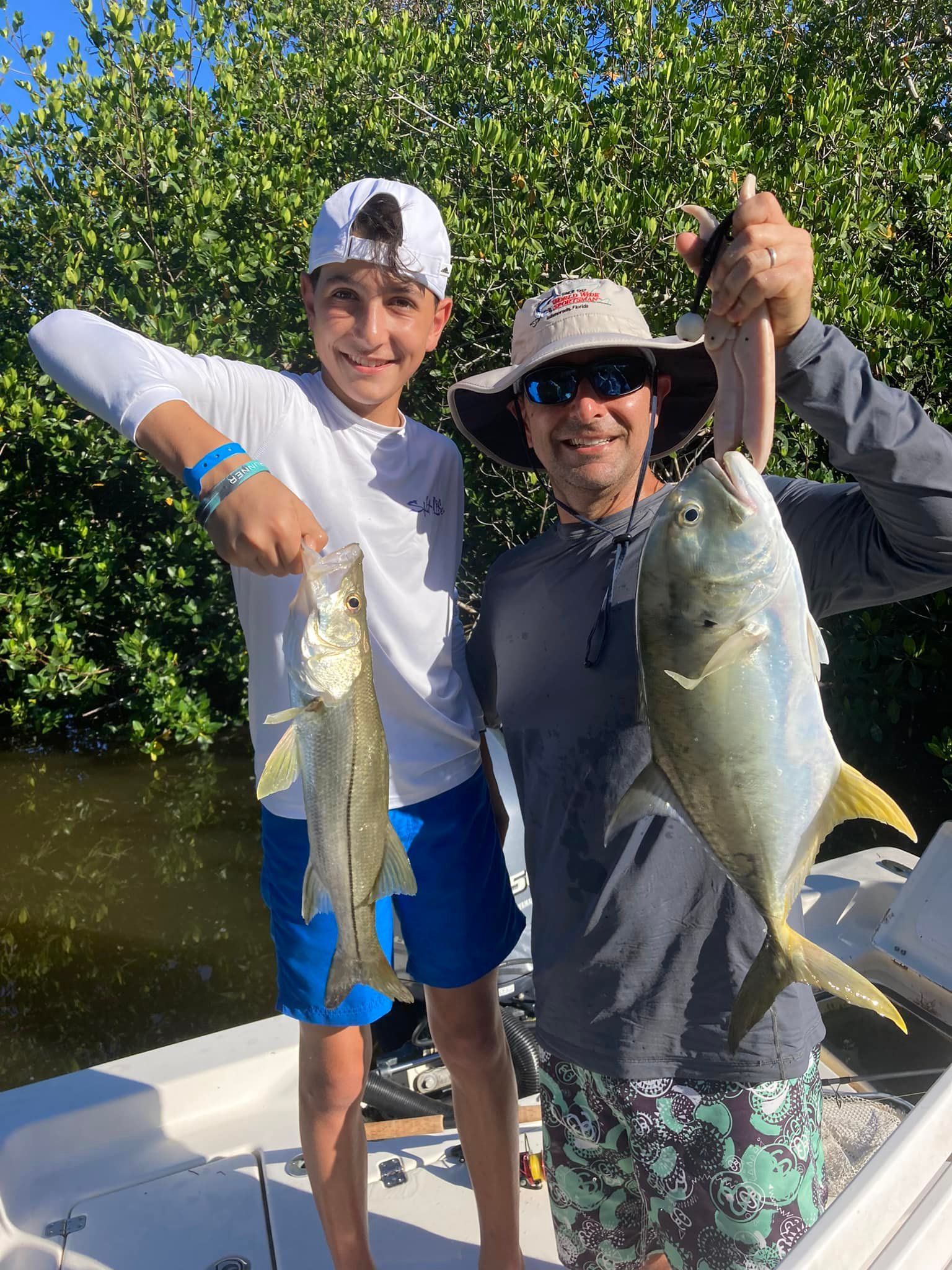 A man and a boy are holding two fish on a boat.