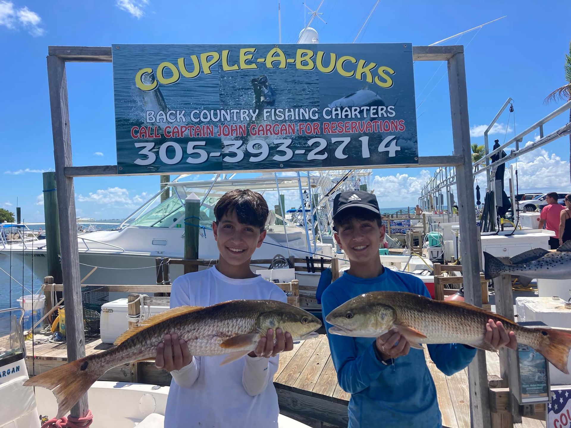 Two boys are holding two fish in front of a couple a bucks sign.