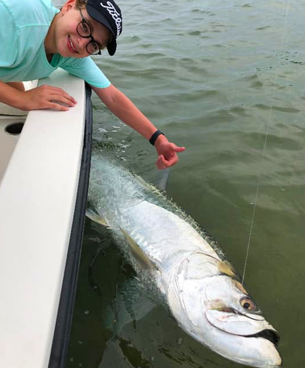 A man wearing a hat that says titleist is reaching for a fish in the water