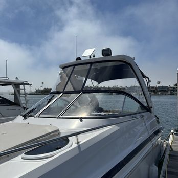 A white motorboat with a clear windshield is docked on a sunny day. The background features blue sky and water.