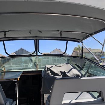 Interior view of a boat cockpit with windows overlooking houses and a blue sky. A seat is covered by a gray tarp.