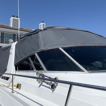 A close-up of a white boat with a dark gray canvas covering the windshield and cabin. The boat is in a sunny outdoor setting.