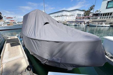 A covered boat docked in a marina with other boats and buildings in the background under a sunny sky. — Boat Canvas in Costa Mesa, CA