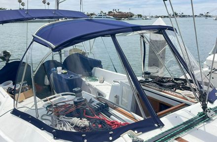 A blue-topped sailboat with clear windows and ropes, docked in a harbor. The boat is white and has a radar antenna. — Boat Canvas in Costa Mesa, CA