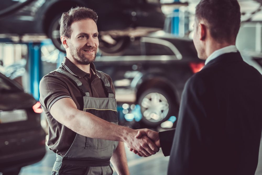 A Man In A Suit Is Shaking Hands With A Mechanic In A Garage — Canberra AutoCare In Fisher, ACT
