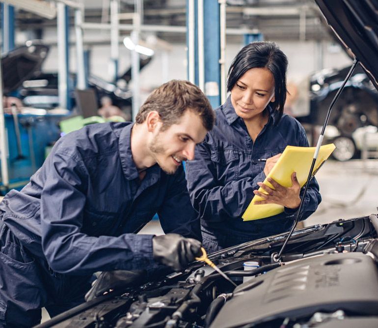 A Man And A Woman Are Working On A Car In A Garage — Canberra AutoCare In Fisher, ACT