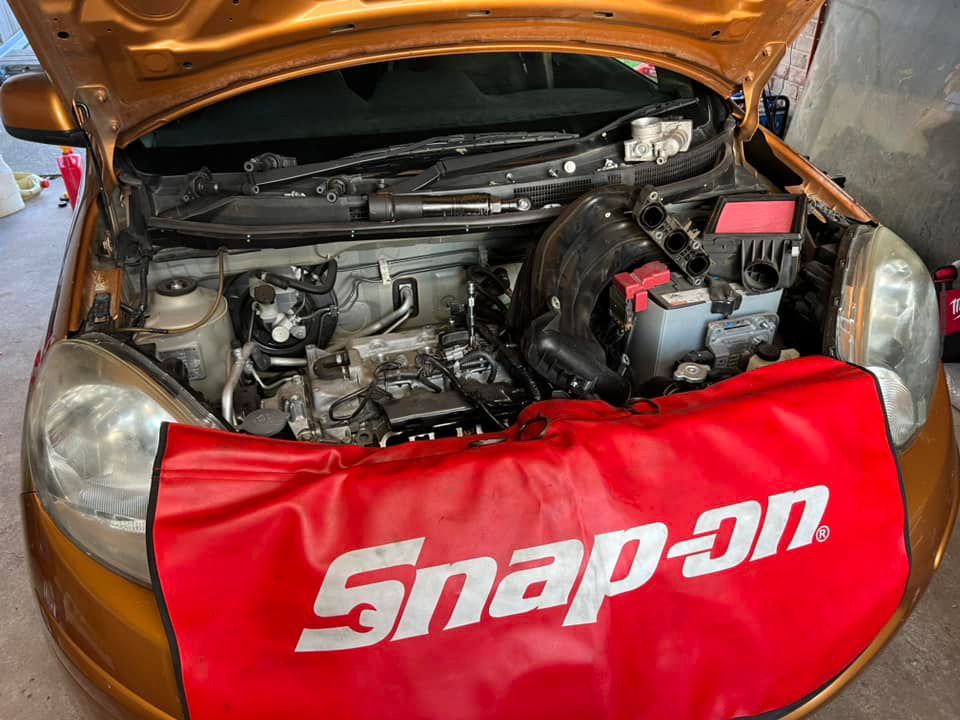 A Man Is Working On A Car Engine With The Hood Open— Canberra AutoCare In Fisher, ACT