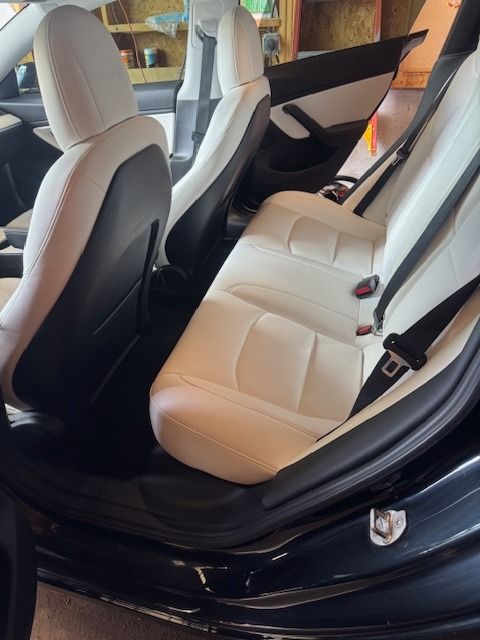 White leather car seats in a black vehicle interior; open door, indoor setting.