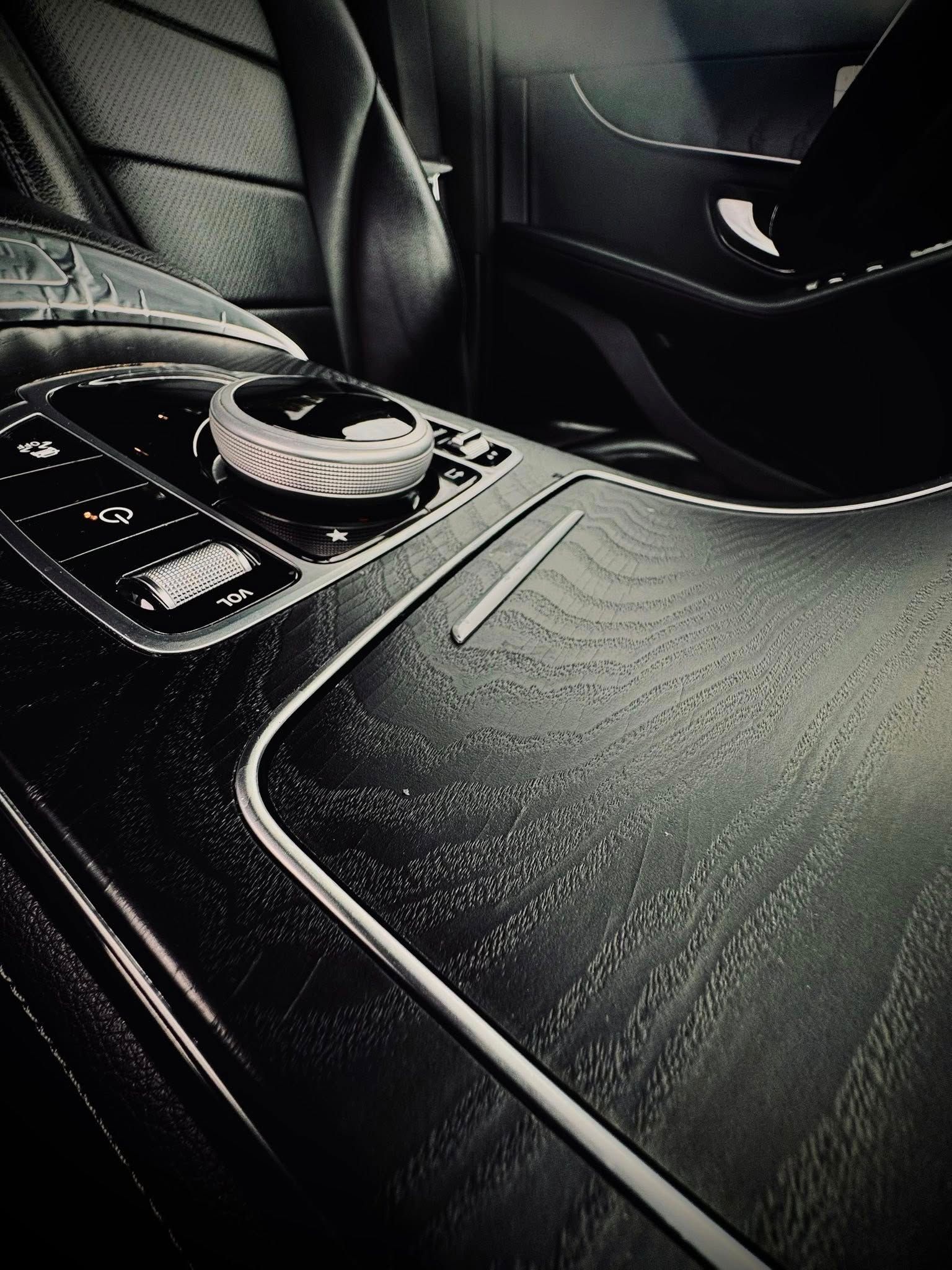 Dark, luxurious car interior: wooden console with controls and a rotary dial. Seats are leather.