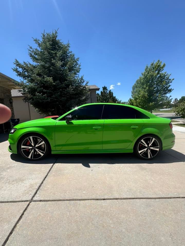 Bright green Audi sedan parked on a driveway, under a blue sky.