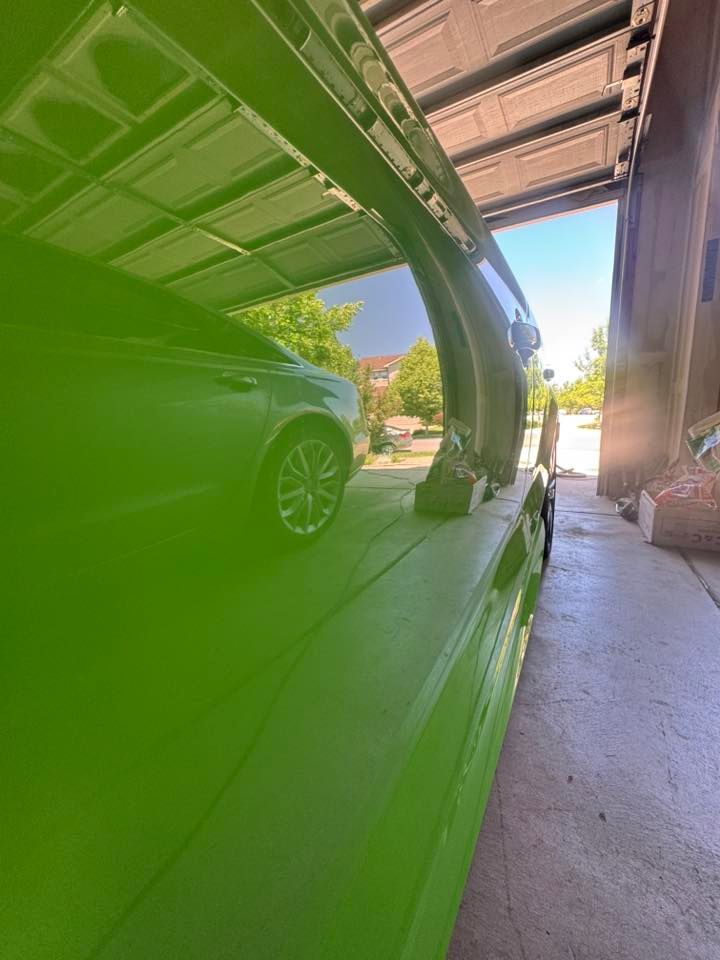 Bright green car with open gullwing door, under a covered area, sunlight visible.