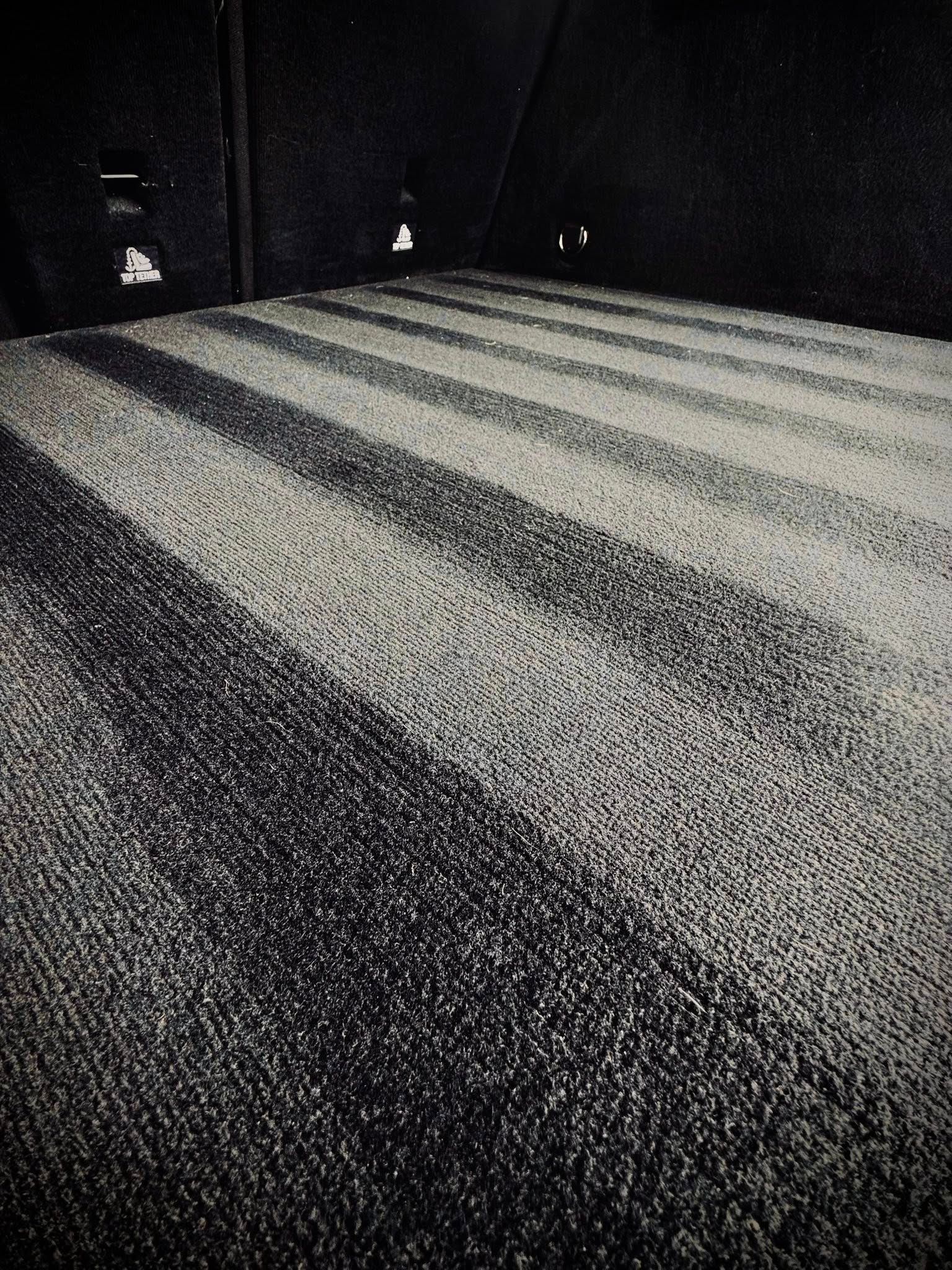 Interior of a dark vehicle bed with a ridged carpet, creating a pattern of black and white stripes.