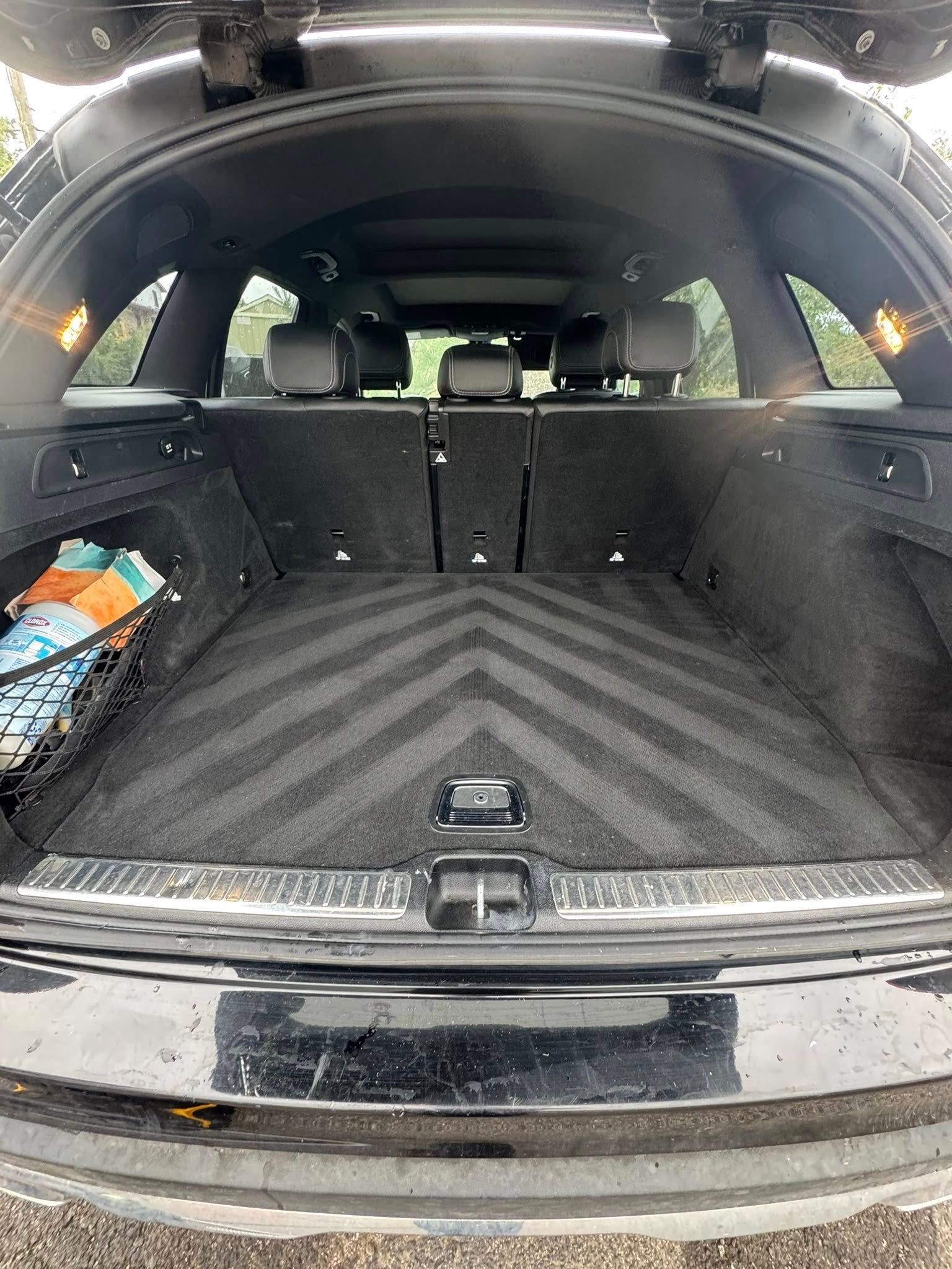 Open black SUV cargo area with dark gray carpet, herringbone pattern, and storage net with items.