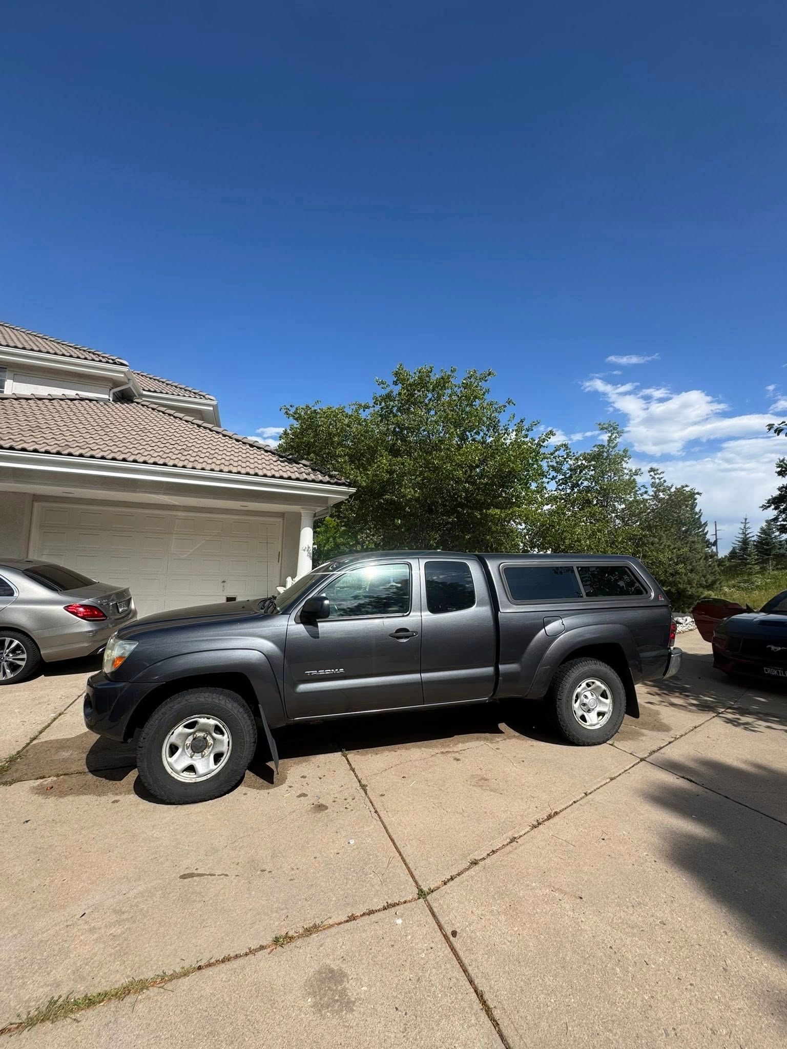 Gray pickup truck with a camper shell parked in a driveway on a sunny day.