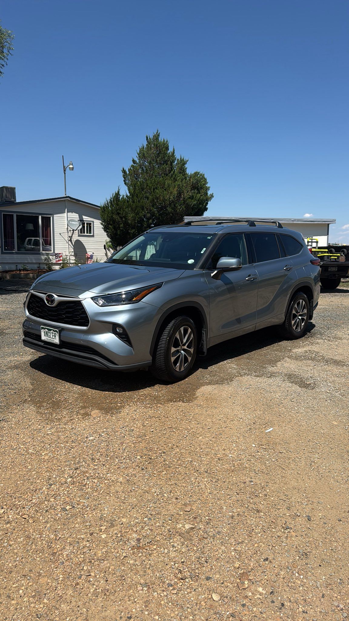 Silver Toyota Highlander SUV parked on gravel under a clear blue sky.