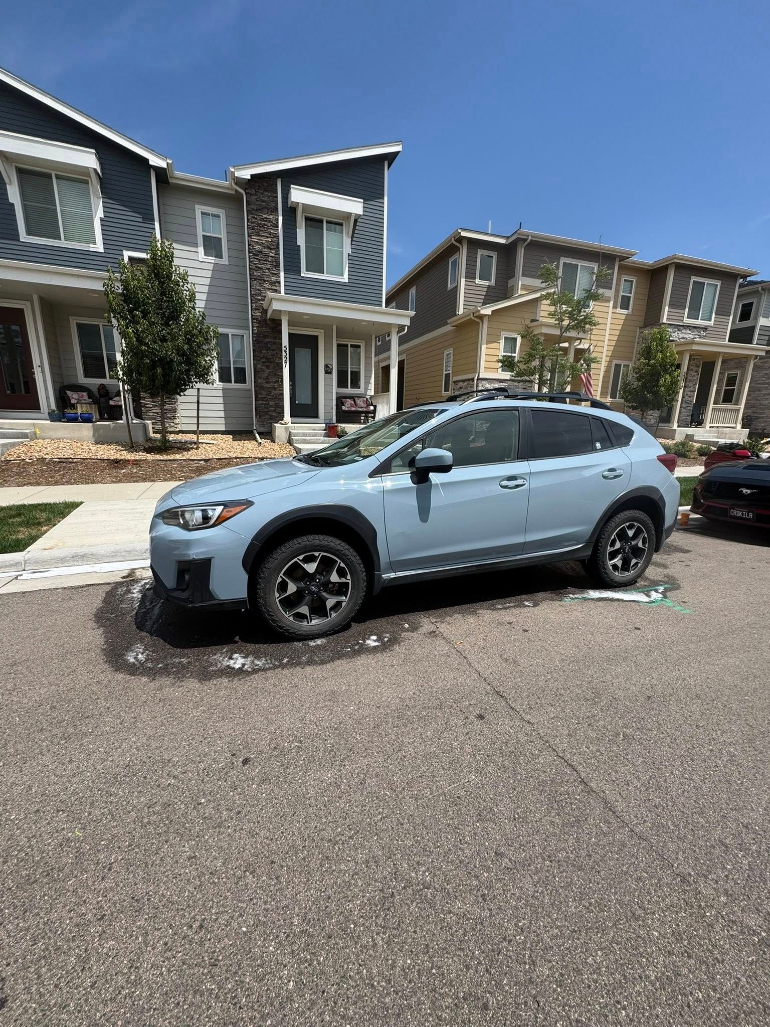 A blue Subaru Crosstrek parked on a paved street in front of townhouses on a sunny day.