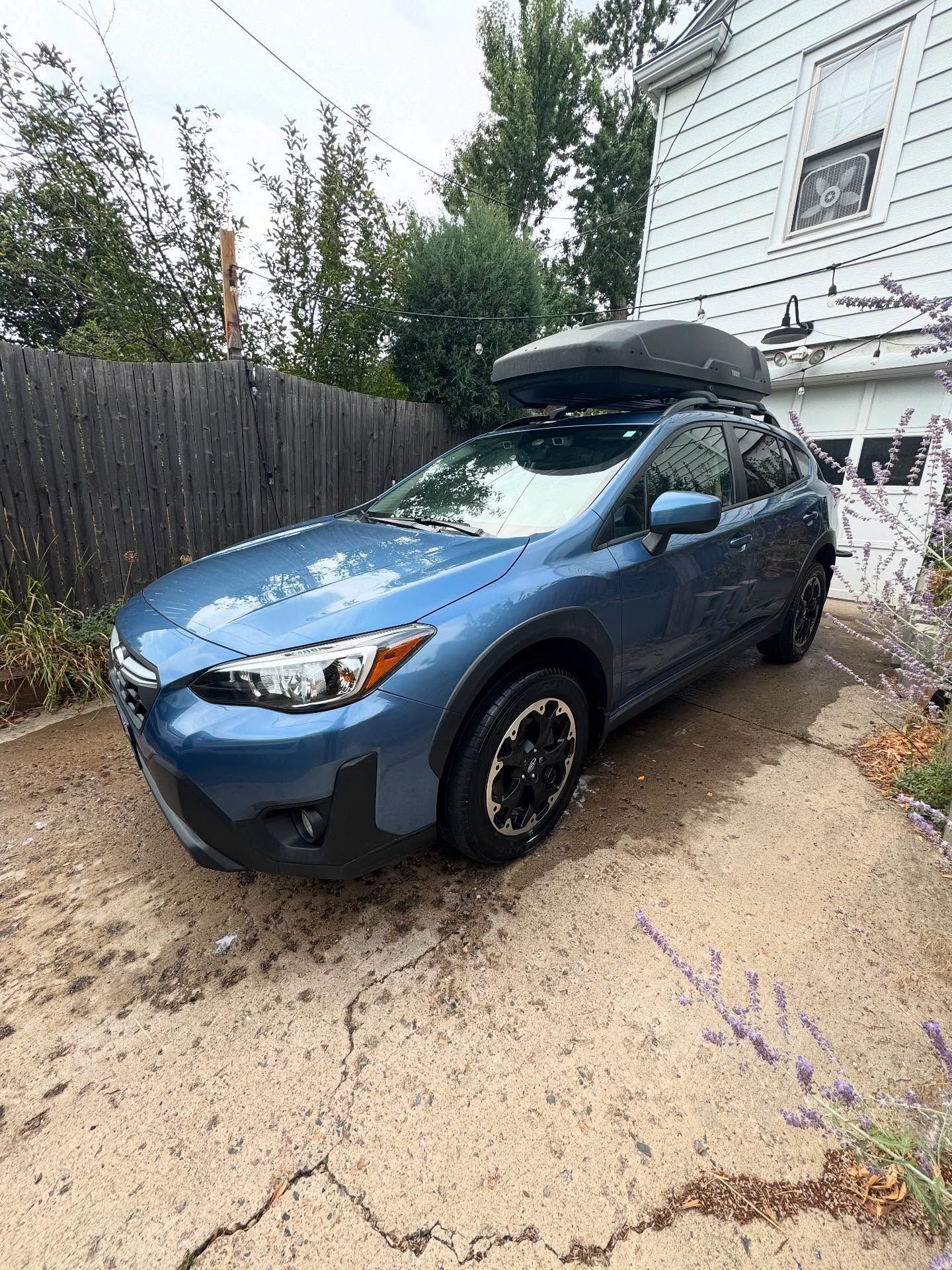 Blue Subaru Crosstrek parked in a driveway, with a black cargo carrier on top.