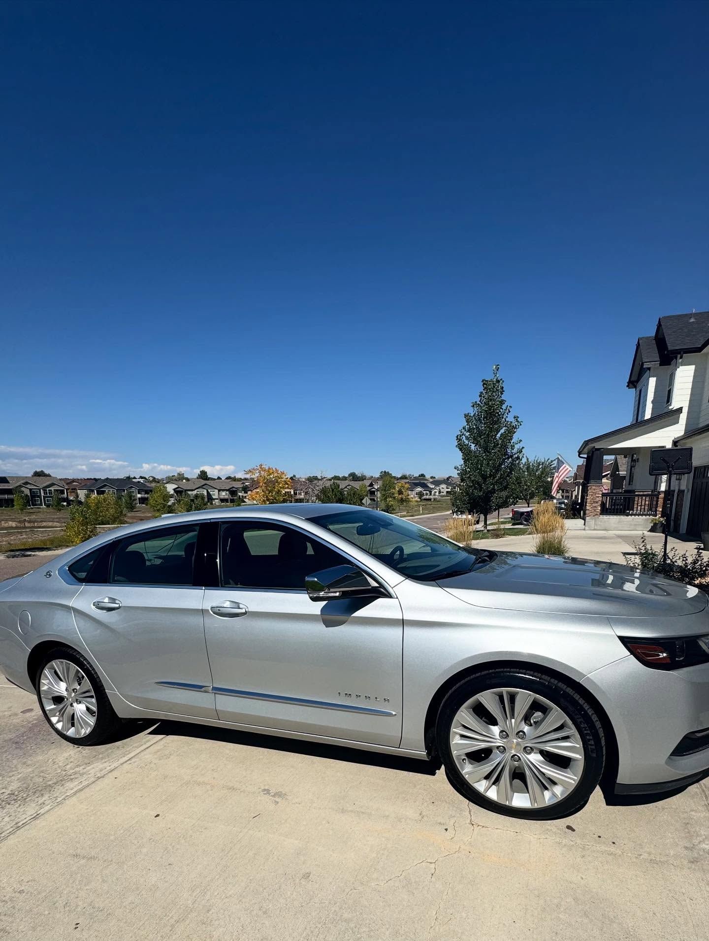 Silver sedan parked in front of a house on a sunny day with a blue sky.