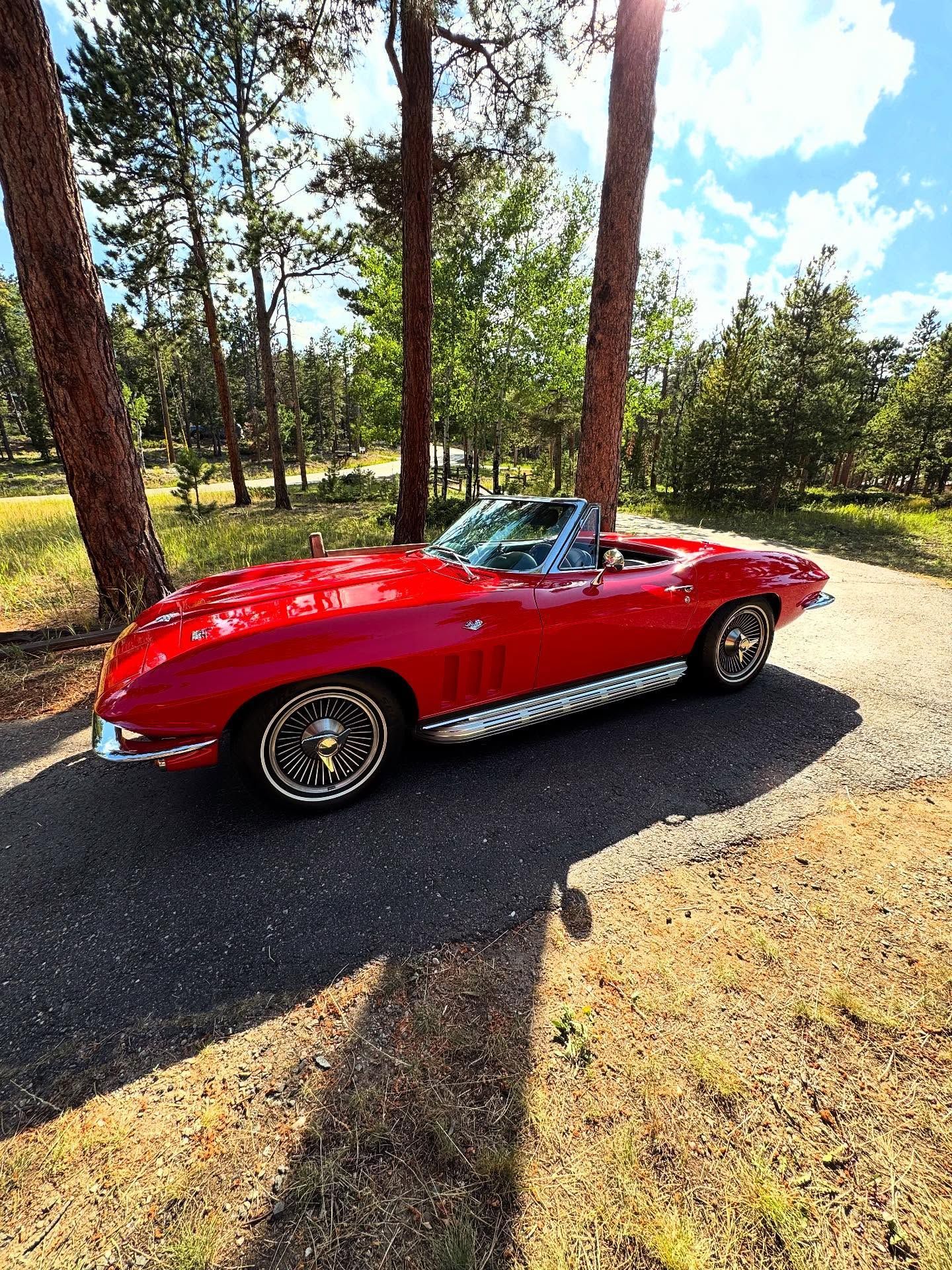 Red convertible sports car parked on a paved path near trees in a sunny outdoor setting.