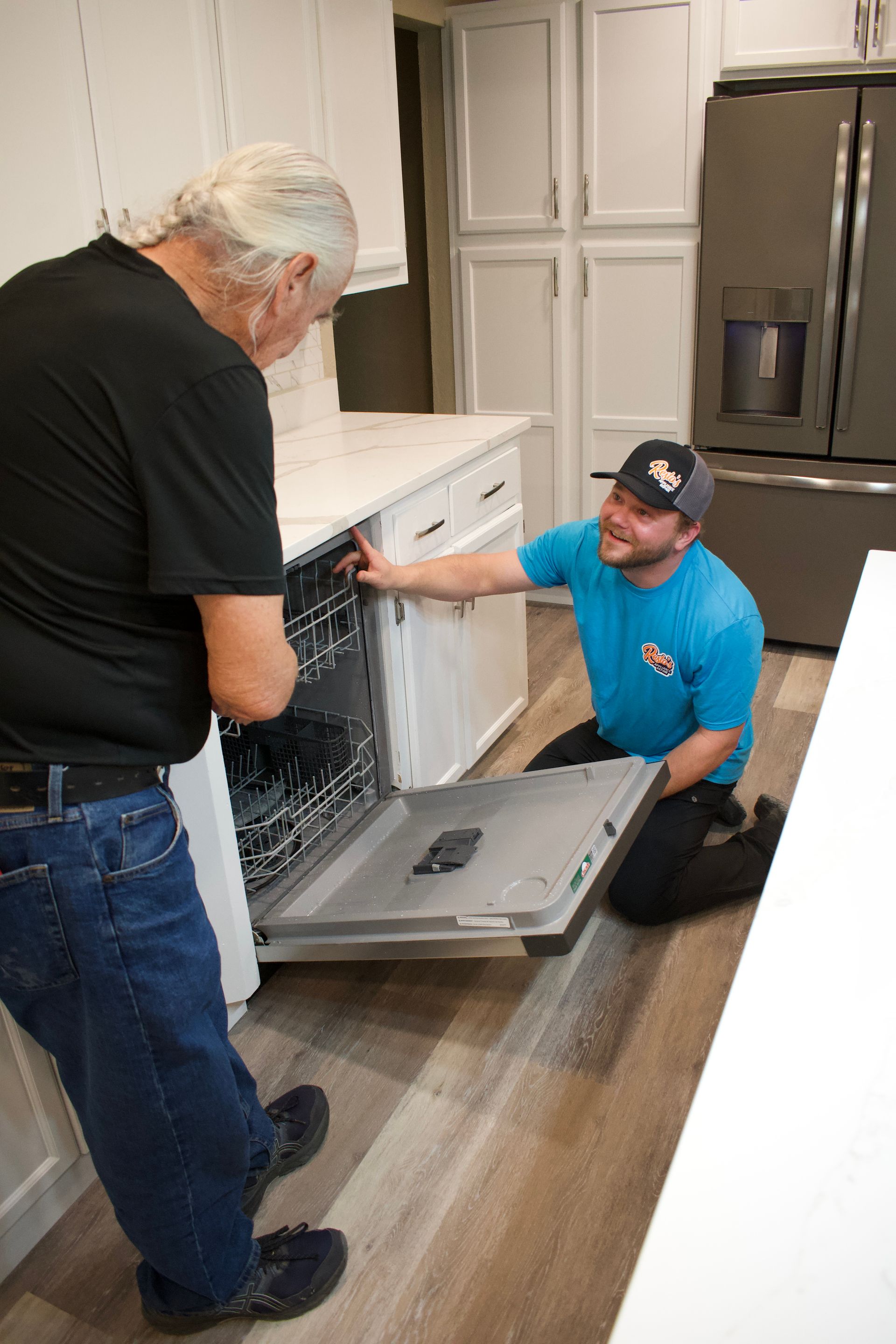 Two men installing a dishwasher in a modern kitchen, one kneeling and one standing.