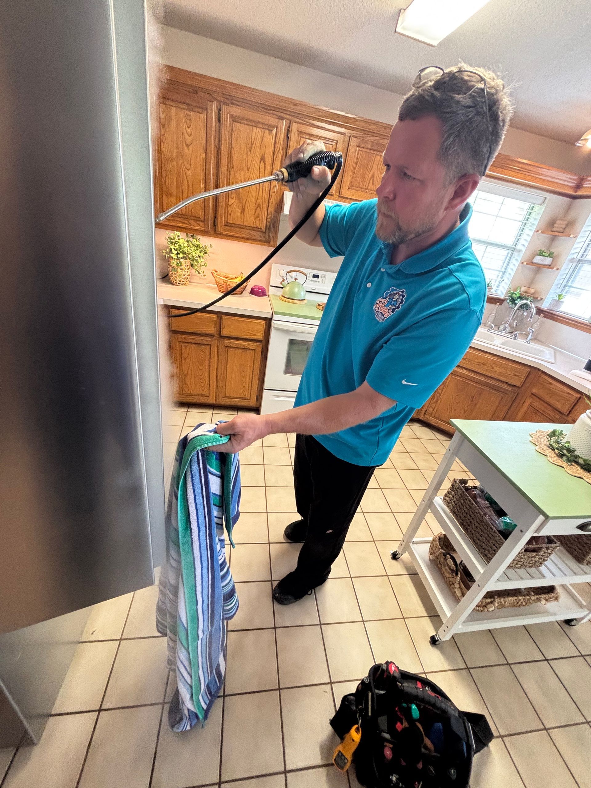 Person cleaning a kitchen floor with a mop beside a bucket and vacuum cleaner.