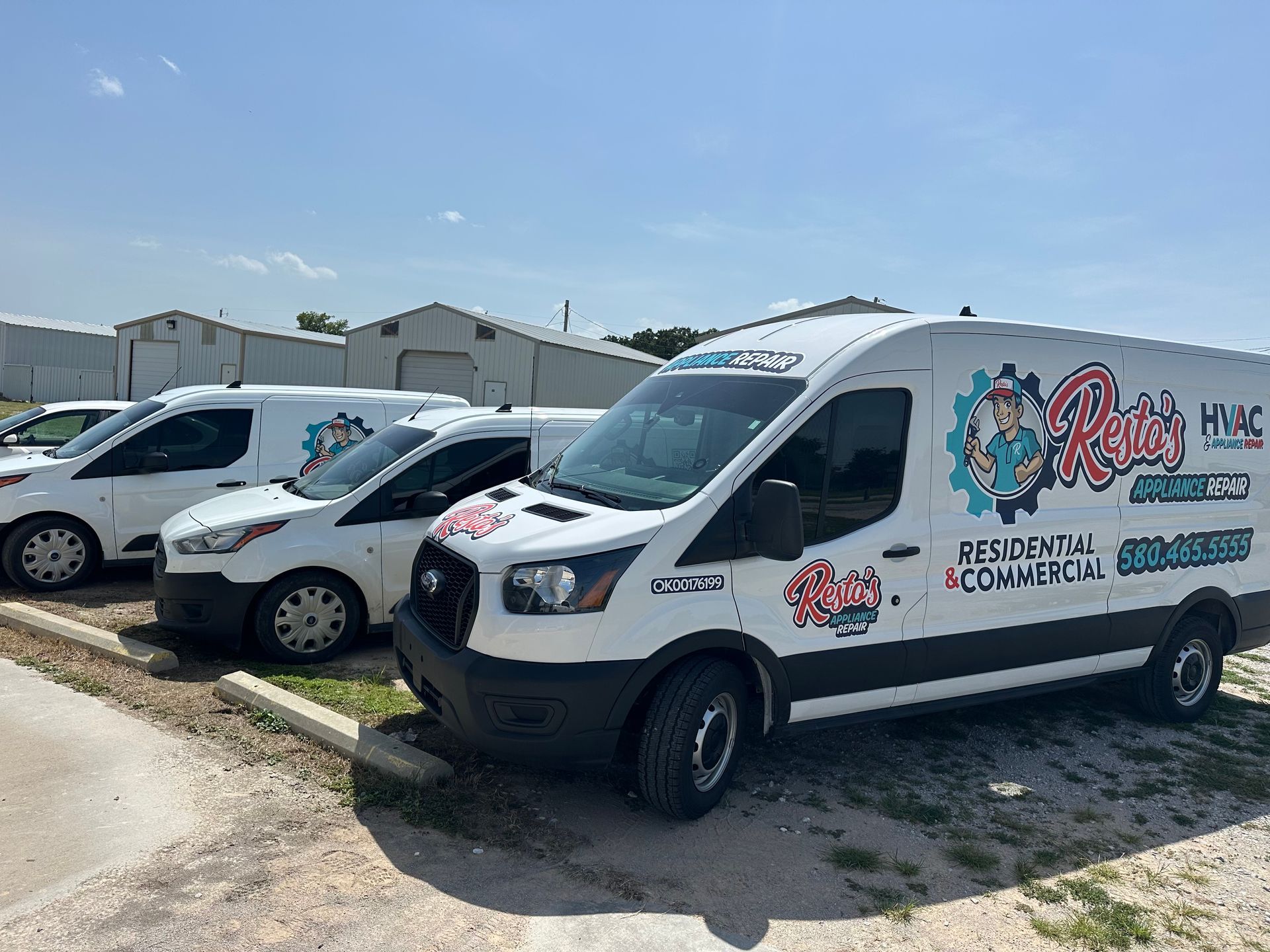 White branded service vans parked in a row on a sunny street near low buildings.