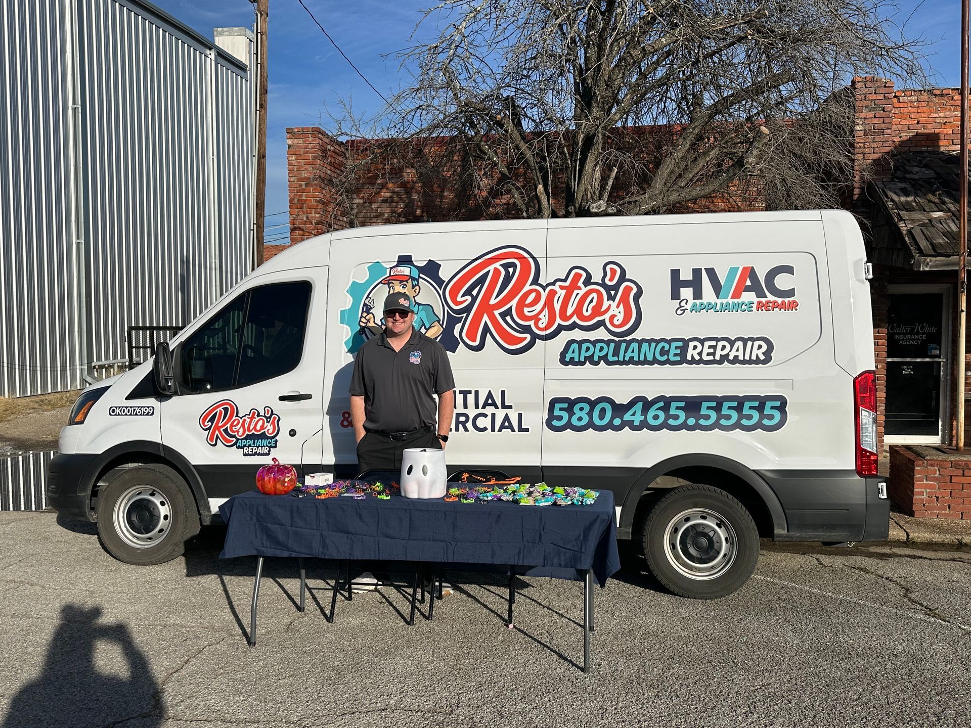 Man posing beside a Resto’s HVAC service van at an outdoor event, with a table in front.