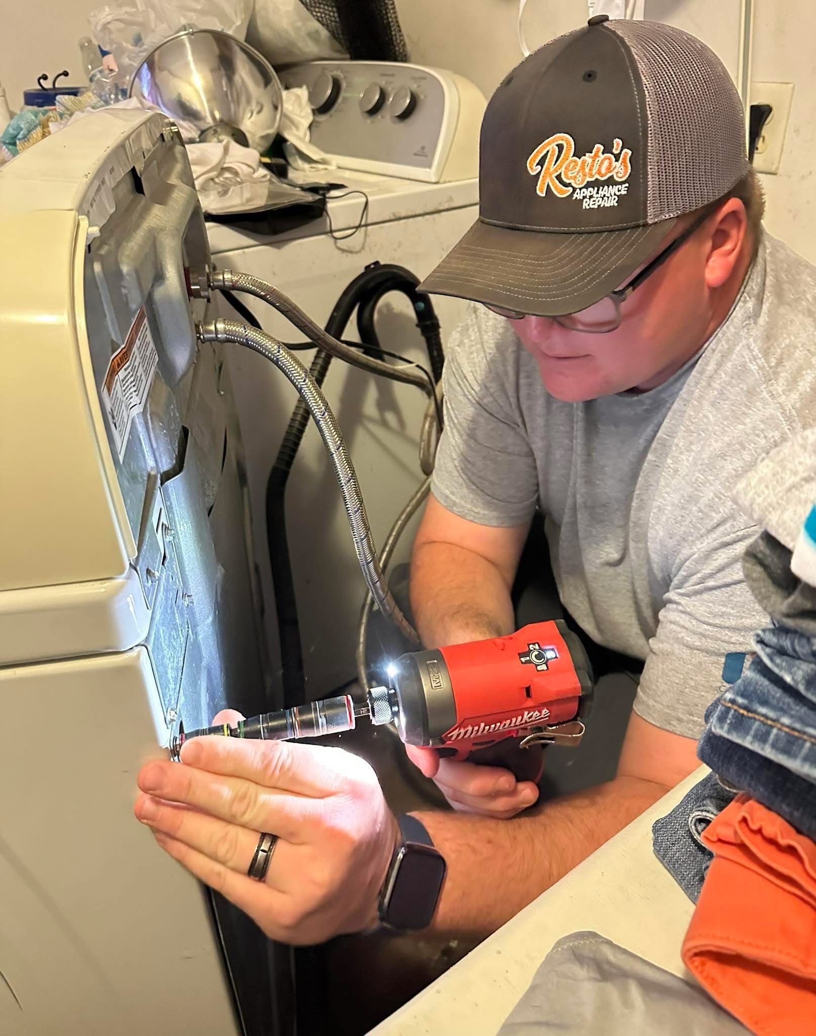 Person using a red tool to work on a laundry appliance inside a laundry room