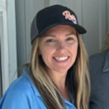 Smiling woman in a black cap and blue shirt standing indoors by a doorway