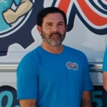 Man in blue T-shirt standing in front of a colorful mural, looking at the camera.