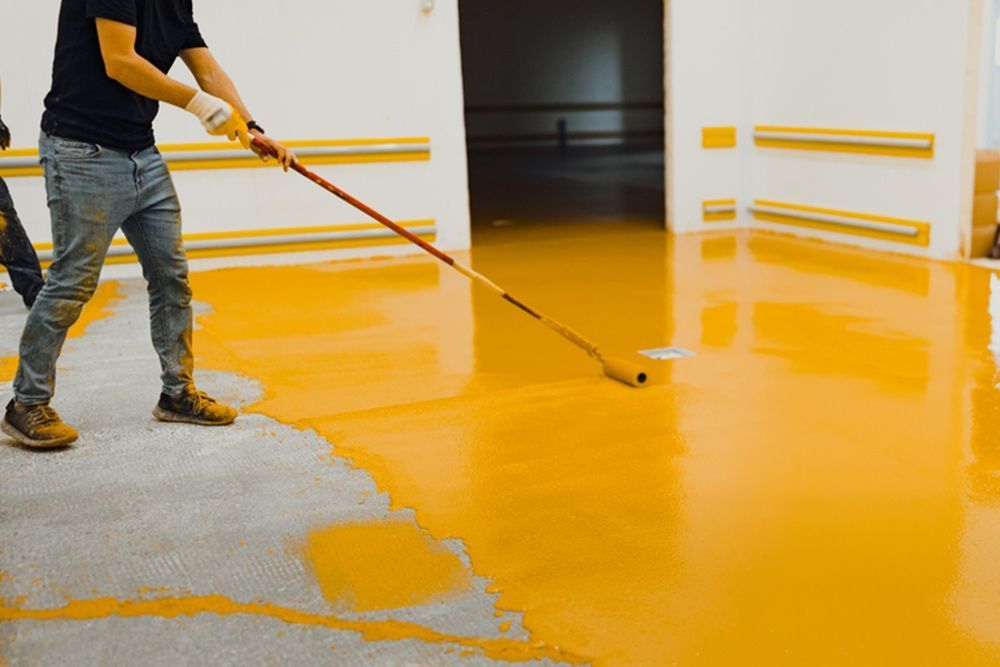 Man using long paint roller to colour the floor yellow — Epoxy Flooring in Fraser Coast, QLD