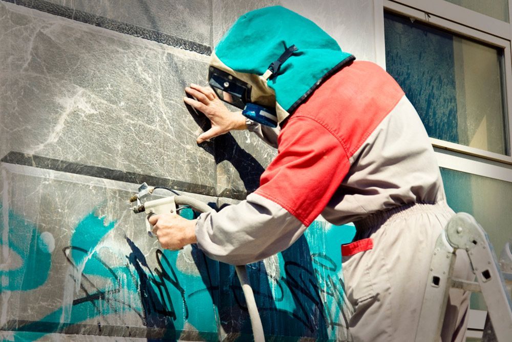 Man using spray gun to paint over graffiti — Epoxy Flooring in Fraser Coast, QLD