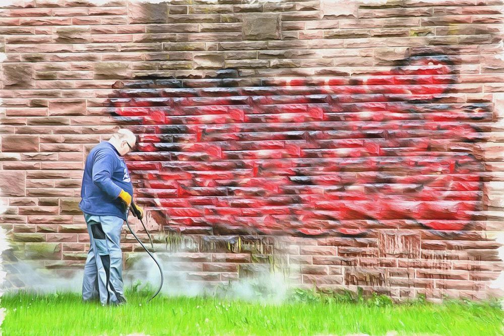 Man using paint sprayer to remove graffiti from a brick wall — Interior Painting in Hervey Bay, QLD