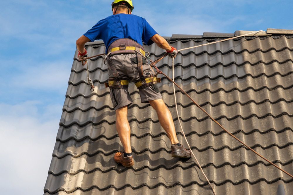 Man with safety equipment painting the roof of a house — Interior Painting in Maryborough, QLD