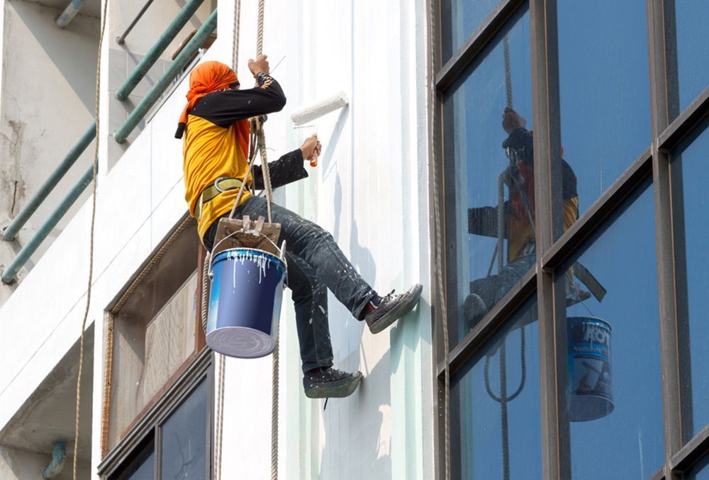 Painter suspended from a harness is painting the exterior wall of the building — Painters in Fraser Coast, QLD