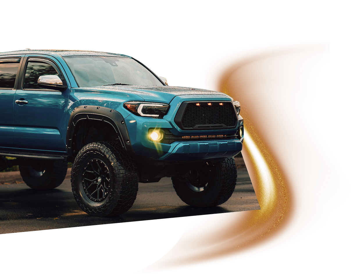 A lifted blue Toyota Tacoma truck with black aftermarket wheels and a custom grille, set against a white background. | J's Automotive