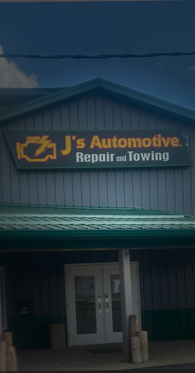 A gray industrial building with a red vehicle parked under a covered entrance on the right side. | J's Automotive