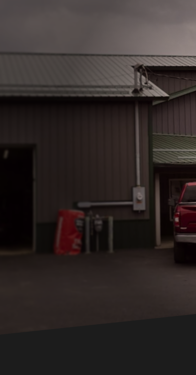 A gray industrial building with a red vehicle parked under a covered entrance on the right side. | J's Automotive