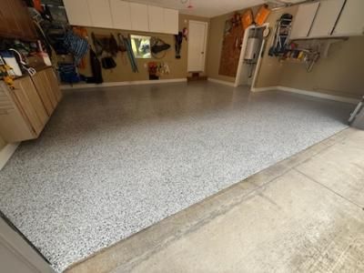 Garage with gray speckled epoxy floor. White cabinets, tools on walls, and a door.