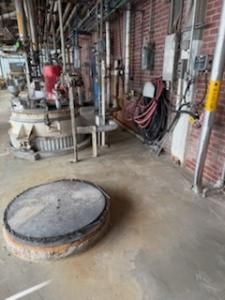 Industrial interior with equipment, brick wall, and a large, round access hatch on the floor.