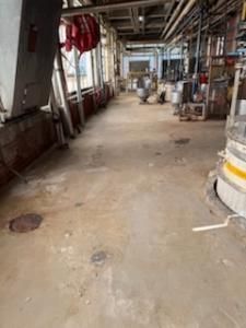 Concrete industrial hallway with pipes, equipment, and sunlight.