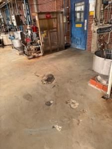 Concrete factory floor with stains, equipment, a metal door, and a blue door.