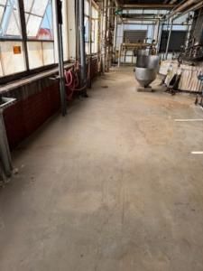 Industrial interior with concrete floor, windows, and equipment; red heating unit along the wall.