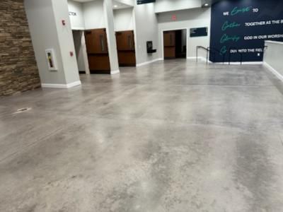 Polished concrete floor in a modern building lobby with doors, a wall with a mural, and a stone accent wall.