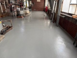 Gray, polished concrete floor in an industrial space with brick walls, windows, and equipment in the background.