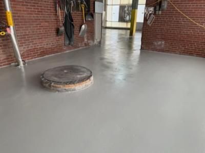 Gray epoxy floor in a brick-walled room with tools hanging on the wall and a circular manhole cover.